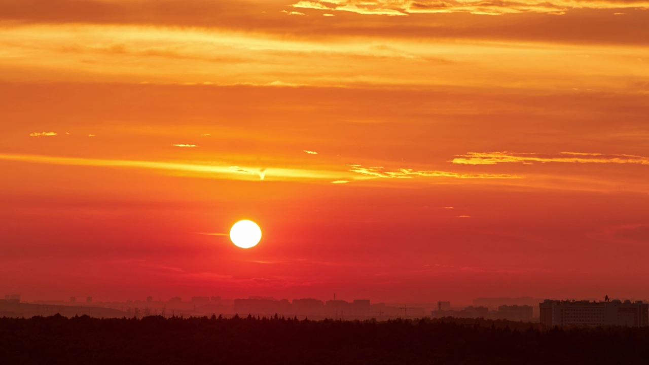 一轮红艳艳的大太阳在夕阳的天空中掠过建筑物的屋顶，城市的风景。傍晚的天空在明亮的阳光下笼罩着黄昏的城市视频素材