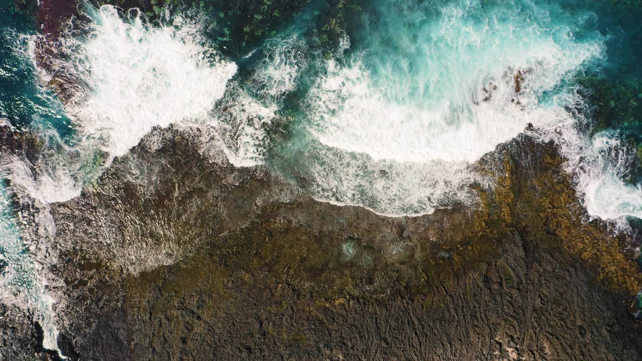 海浪在空旷的多岩石的热带海滩上拍打着泡沫，海滩上有巨大的火山构造和石头。狂野的海滩遇见深蓝色的碧水。从上面俯瞰巨大的海洋。视频素材