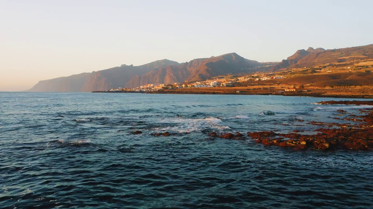 火山岩石海滩，日落。大海波涛平静，海水蔚蓝。探索世界。特内里费。西班牙加纳利群岛。美丽的城市风光，度假小镇。旅行上瘾。空中静态视图。视频素材