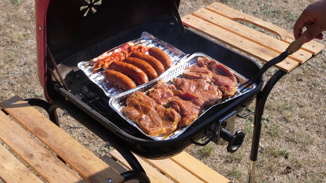 一个人在炎热的夏天打开一个花园烧烤架，检查里面的肉视频素材