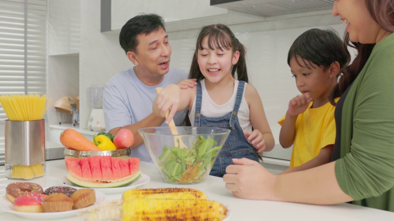 幸福的家庭一起烹饪，父母教孩子，儿子，女儿准备新鲜的蔬菜沙拉和羊角面包在现代厨房内部生产营养晚餐视频素材