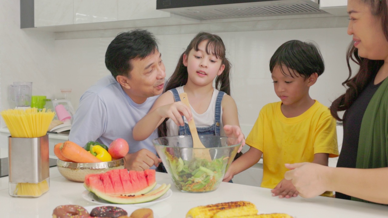 幸福的家庭一起烹饪，父母教孩子，儿子，女儿准备新鲜的蔬菜沙拉和羊角面包在现代厨房内部生产营养晚餐视频素材