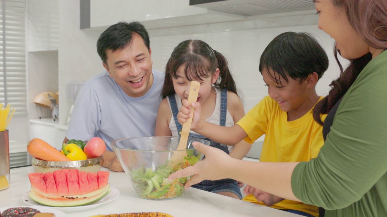 幸福的家庭一起烹饪，父母教孩子，儿子，女儿准备新鲜的蔬菜沙拉和羊角面包在现代厨房内部生产营养晚餐视频素材