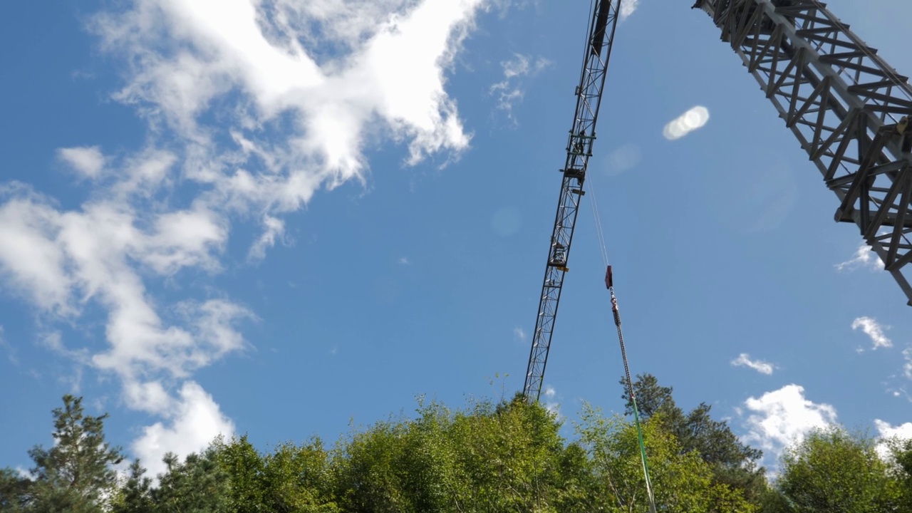 施工现场运载建筑材料的大型建筑起重机。塔吊顶着蓝天白云搬运重物。建筑及发展业视频素材