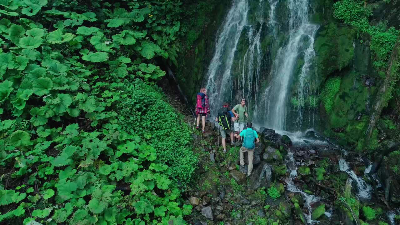 一群科学家在高山瀑布脚下。探险队队长举起北欧人的手杖，庆祝目标的实现。视频下载