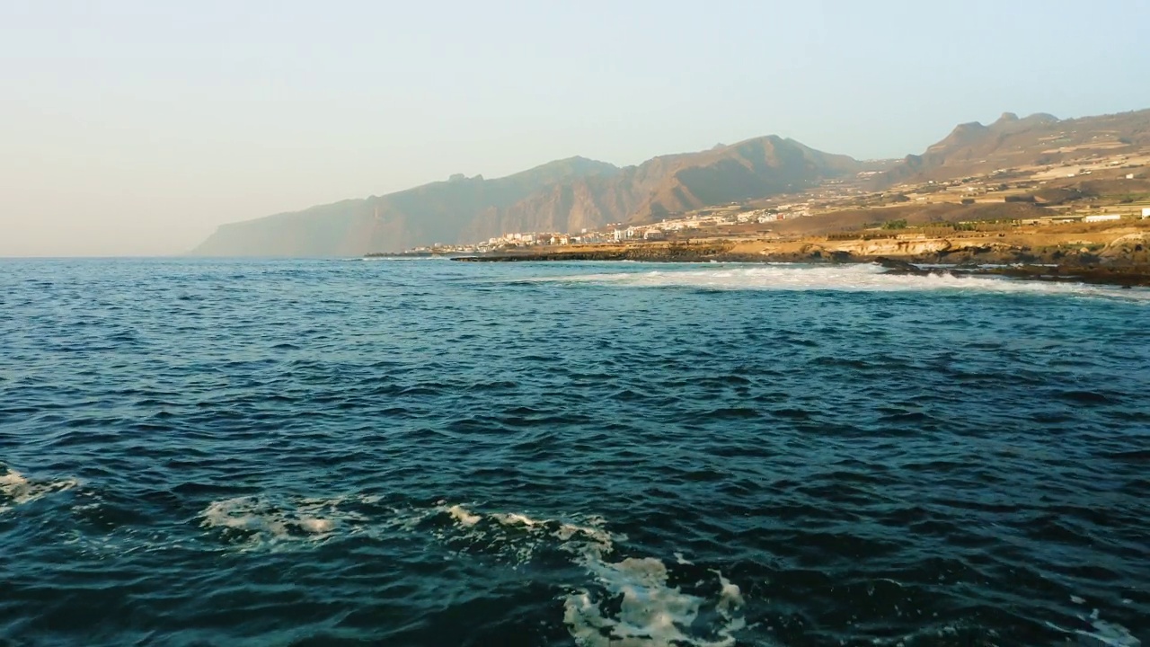 暴风雨天气中在海面低空飞行的无人机。海浪泛起泡沫飞溅。岩石海岸。背景是Los Gigantes悬崖。特内里费。美丽的风景在蓝绿色的大西洋水域。金丝雀。视频素材