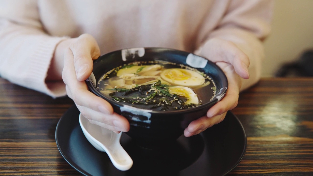 日本餐厅的亚洲菜特写。女人的手端着一盘鸡肉味增汤和一个鸡蛋和面条。视频素材