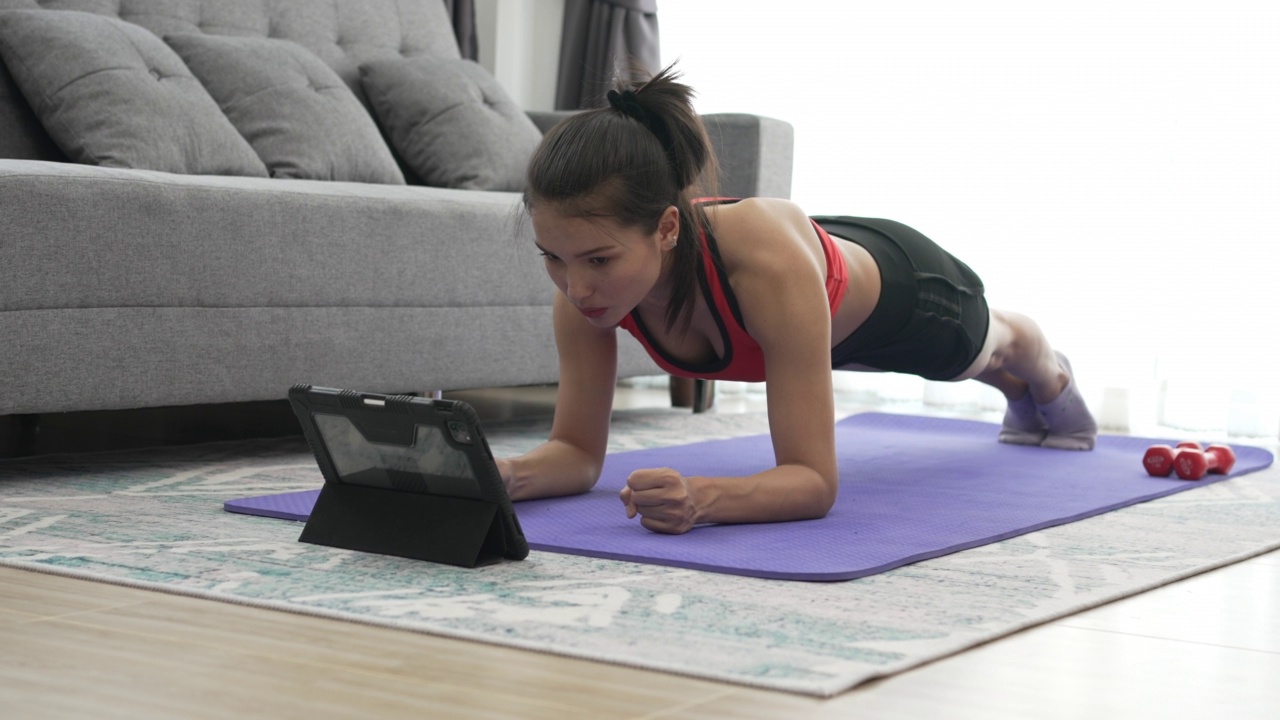 年轻的肌肉健身妇女在客厅地板上的瑜伽垫上做平板运动视频素材