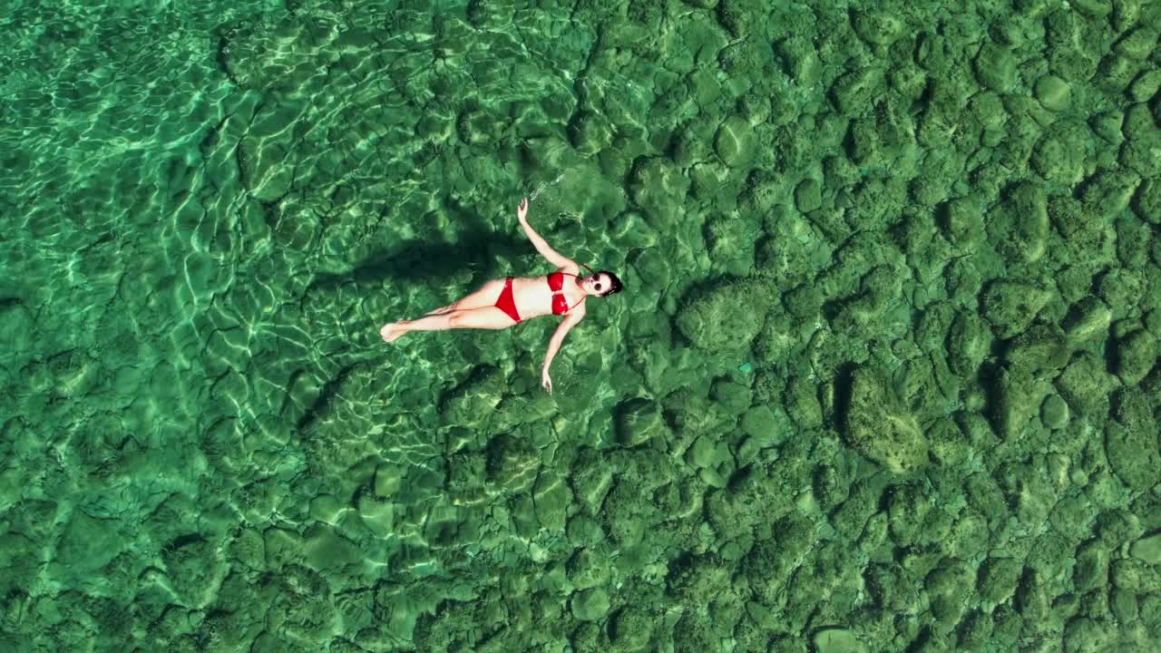 年轻女子漂浮着，放松着。美丽的女人沐浴在绿松石水视频素材