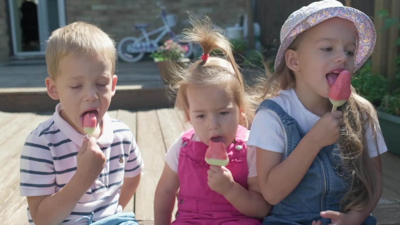 三个可爱的小孩正在享用美味的蛋筒冰淇淋。吃西瓜冰棍的孩子。孩子们兄弟姐妹在家庭花园吃糖果。暑假天气炎热，晴天。童年,食品糖果视频素材