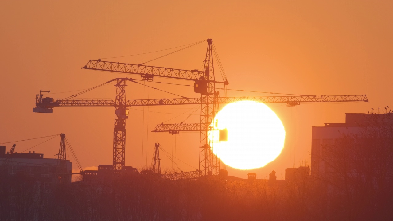 夕阳下高楼公寓建筑工地塔吊的黑色剪影。房地产开发视频素材