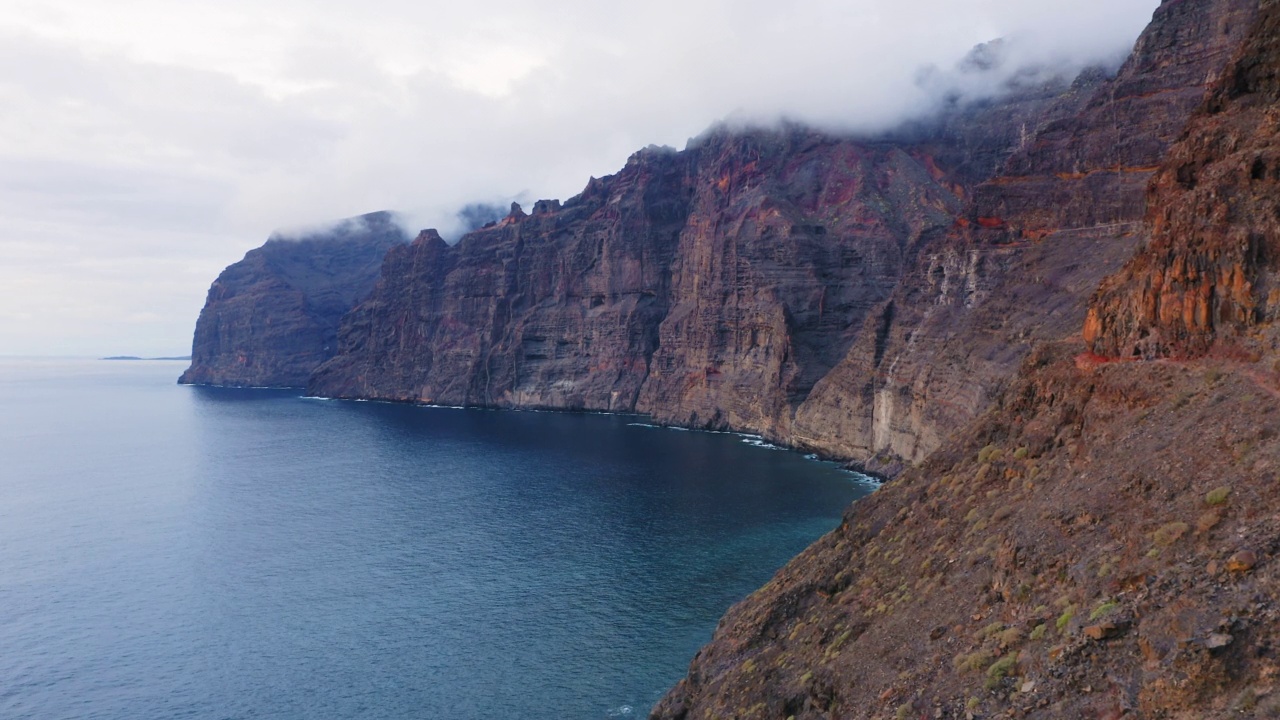 洛杉矶Gigantes。特内里费。加那利岛。西班牙。无人机鸟瞰宁静的海景，开阔的海洋，巨大的悬崖。悲观的多云的天气。蓝色海湾的日落。夏日余晖中湛蓝的海水。视频素材