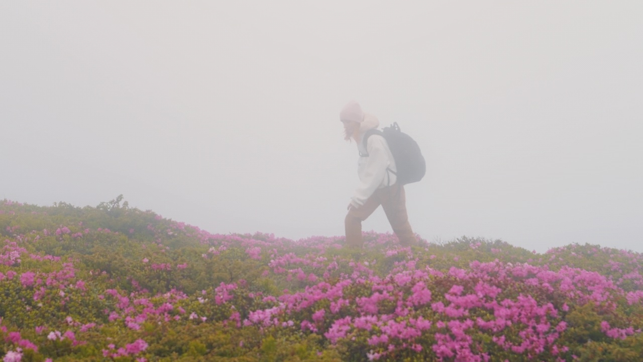 一个女人背着背包在雨天走在山路上。视频素材