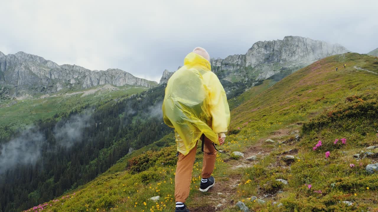 背面的女人走在山的边缘穿着雨衣。视频素材