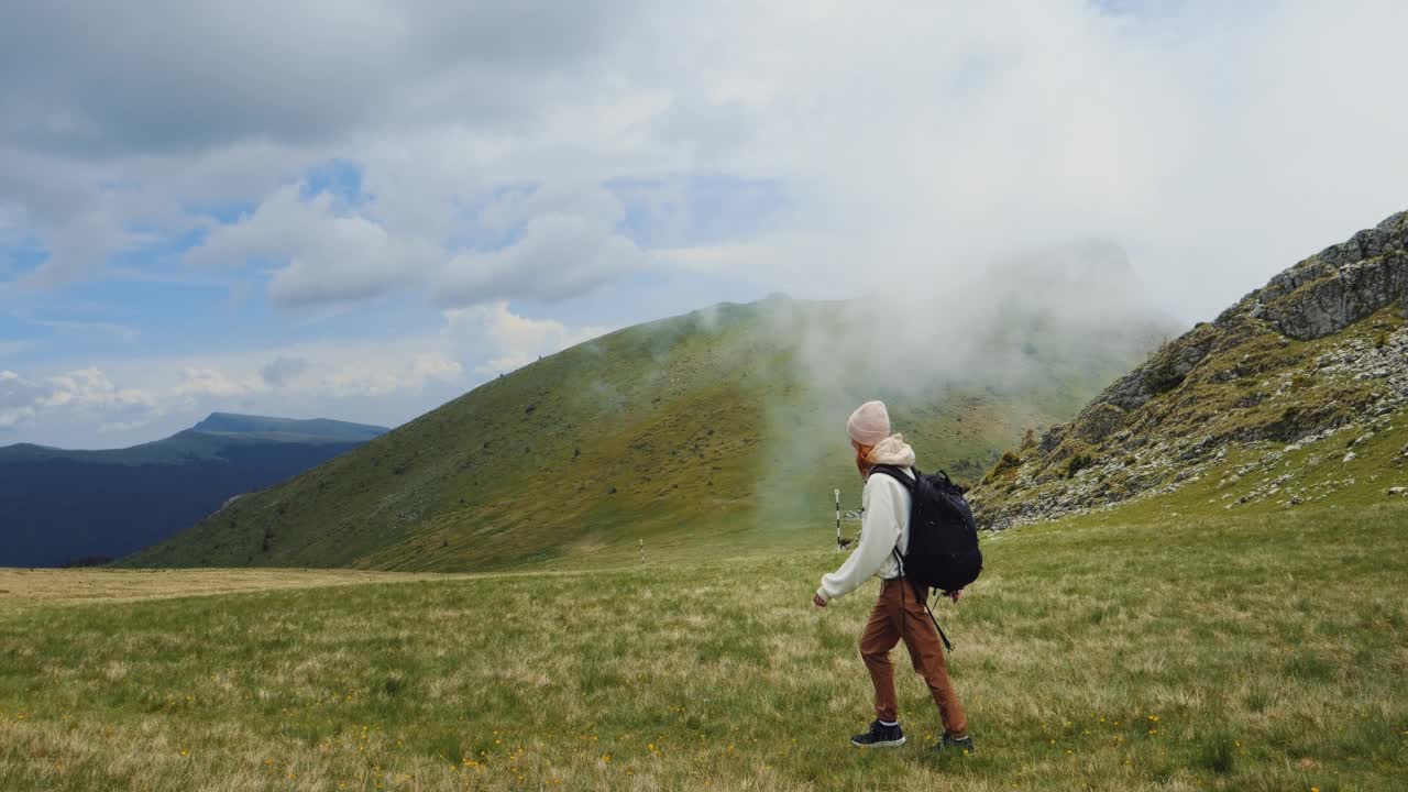 阴天里，女人走在青山的草地上，回头看风景如画。视频素材