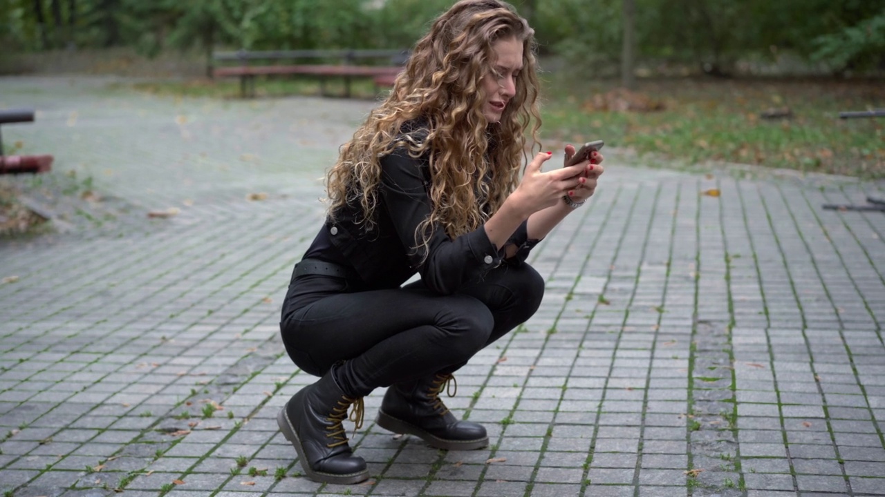 沮丧哭泣的美丽女人坐在公园小巷的hunkers在智能手机上在线消息。广角肖像的悲伤强调焦虑的白人妇女户外在秋天的一天。视频素材