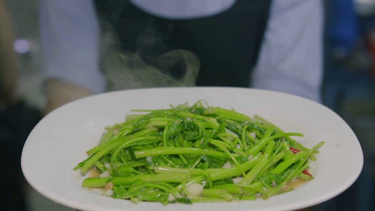 近距离的新鲜烹饪炒热的绿色中国牵牛花或菠菜叶蔬菜与辣椒和大蒜的白色菜，健康的亚洲泰国菜视频素材