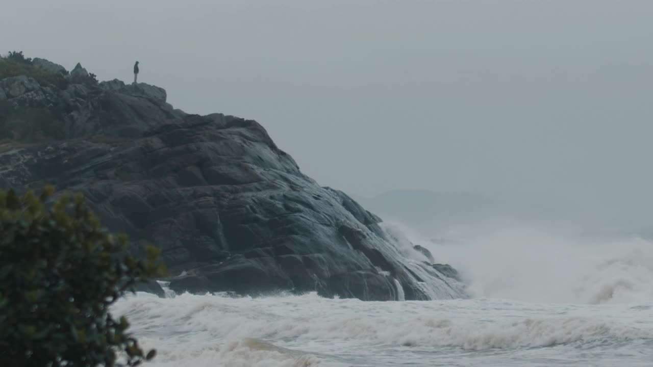 人们站在岩石上，看着海洋风暴期间的巨浪拍打着岩石视频素材