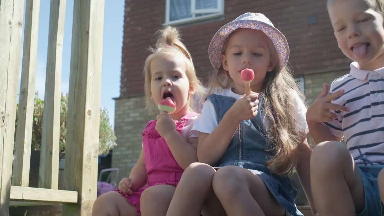 三个可爱的小孩正在享用美味的蛋筒冰淇淋。吃西瓜冰棍的孩子。孩子们兄弟姐妹在家庭花园吃糖果。暑假天气炎热，晴天。童年,食品糖果视频素材