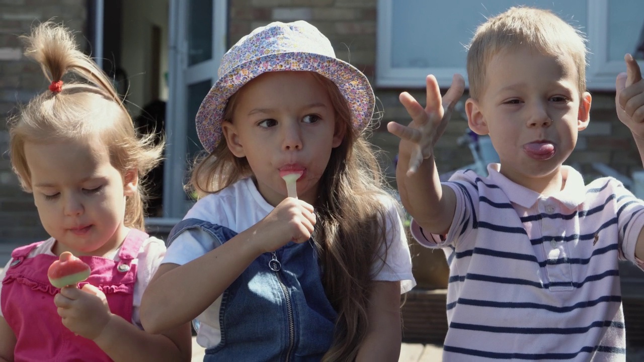 三个可爱的小孩正在享用美味的蛋筒冰淇淋。吃西瓜冰棍的孩子。孩子们兄弟姐妹在家庭花园吃糖果。暑假天气炎热，晴天。童年,食品糖果视频素材