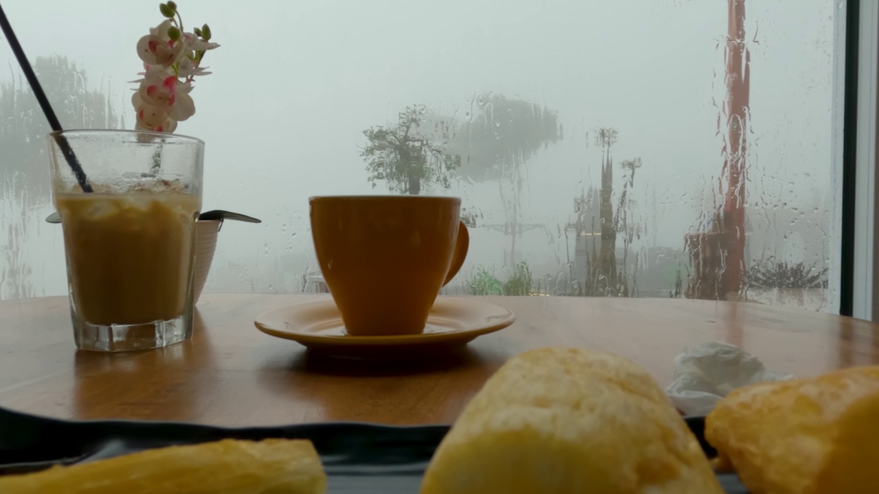 一杯热饮和冰牛奶咖啡，靠近被雨水溅起的窗玻璃视频素材