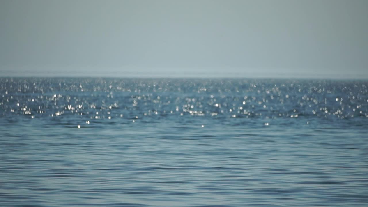 抽象海夏天海洋日落自然背景。水面上的小波浪在太阳的金色散焦光下运动模糊。假日、度假和休闲的概念。慢动作视频素材