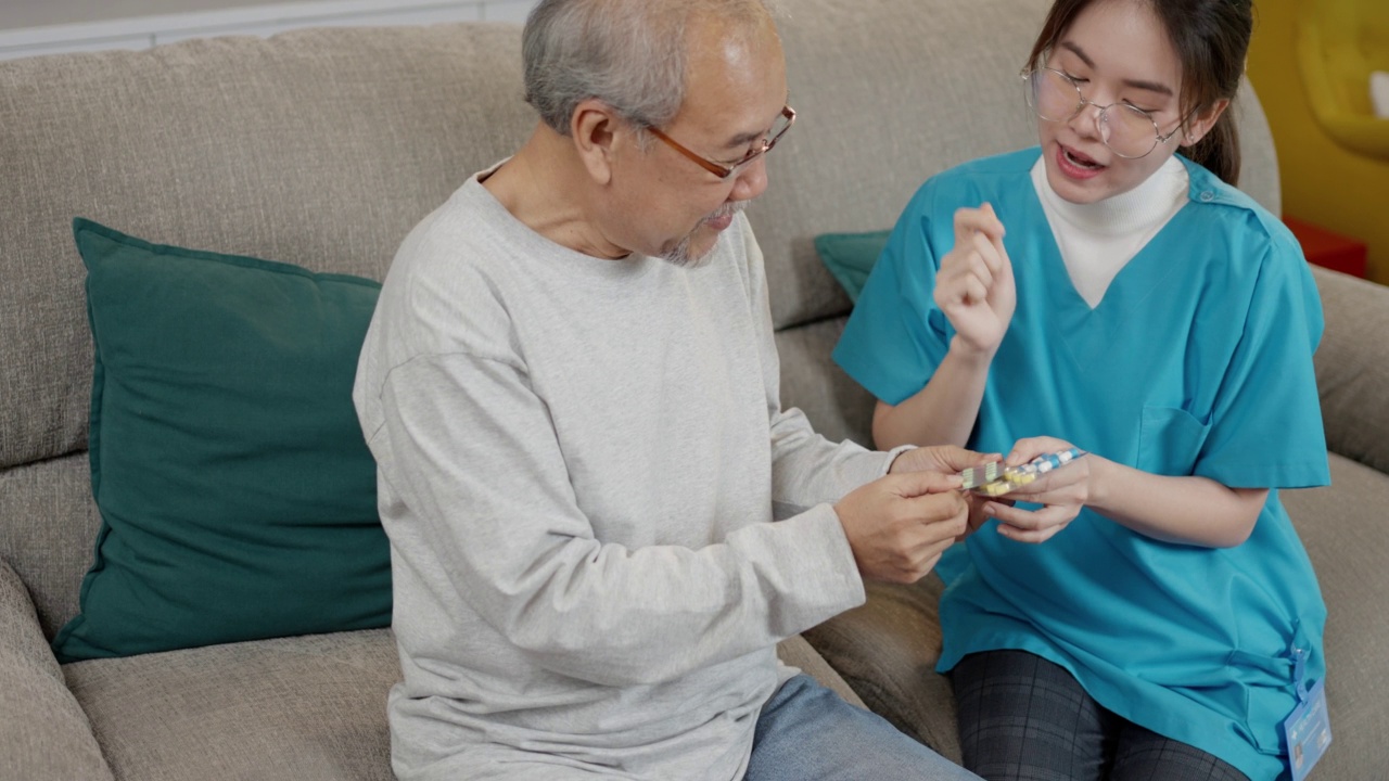 亚洲老年男性患者在敬老院与医生护士咨询处方药。护工治疗师药剂师妇女在客厅里拿着药瓶，药量在家里。视频素材