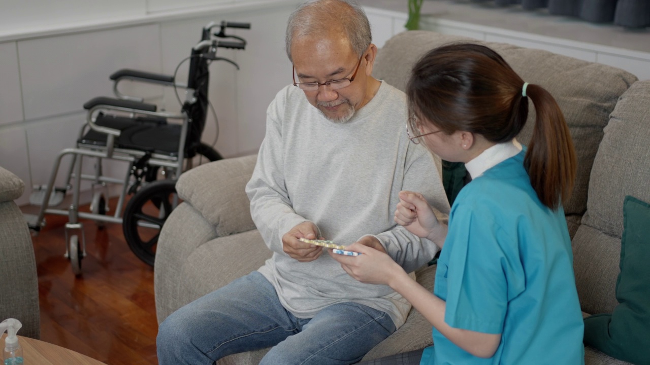 亚洲老年男性患者在敬老院与医生护士咨询处方药。护工治疗师药剂师妇女在客厅里拿着药瓶，药量在家里。视频素材