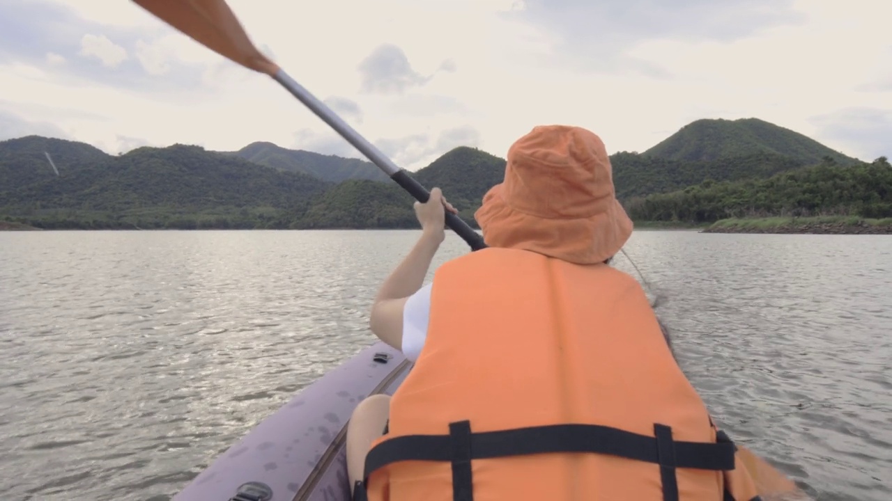 后景迷人的年轻女子划着充气皮艇在水的大山湖。旅游目的地，探险，度假度假的概念。视频素材