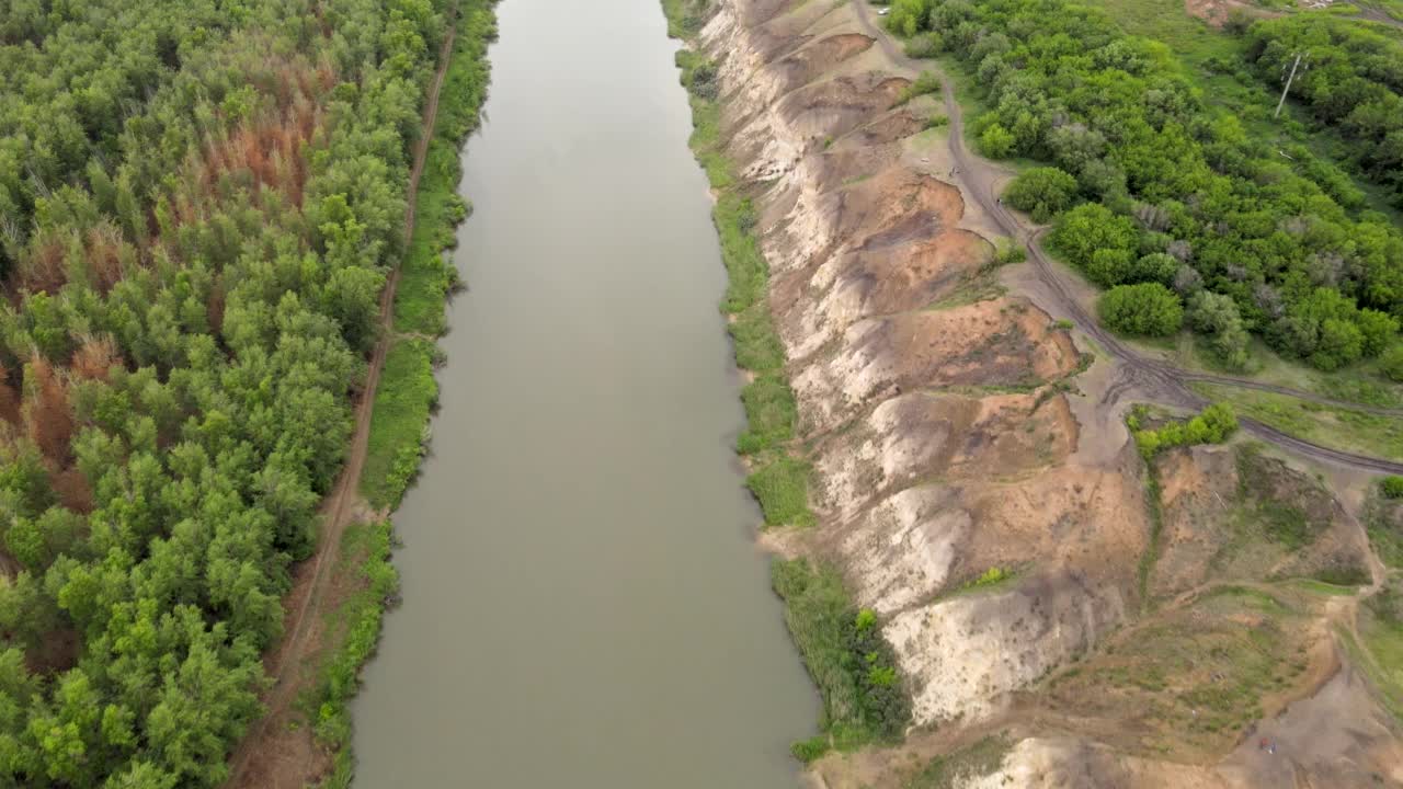 这条河穿过森林。粘土河岸。高的悬崖。河水浑浊。绿色的森林围绕着水。用无人机，四轴飞行器射击。鸟瞰图，令人惊叹的风景。视频下载