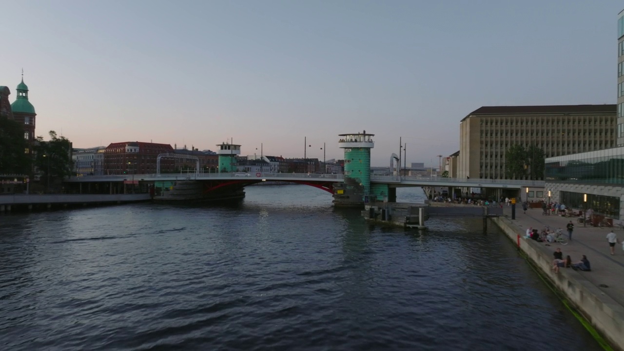 在水面上低空飞行。飞越尼佩尔斯桥，在黄昏时展示海滨的建筑。丹麦哥本哈根视频素材