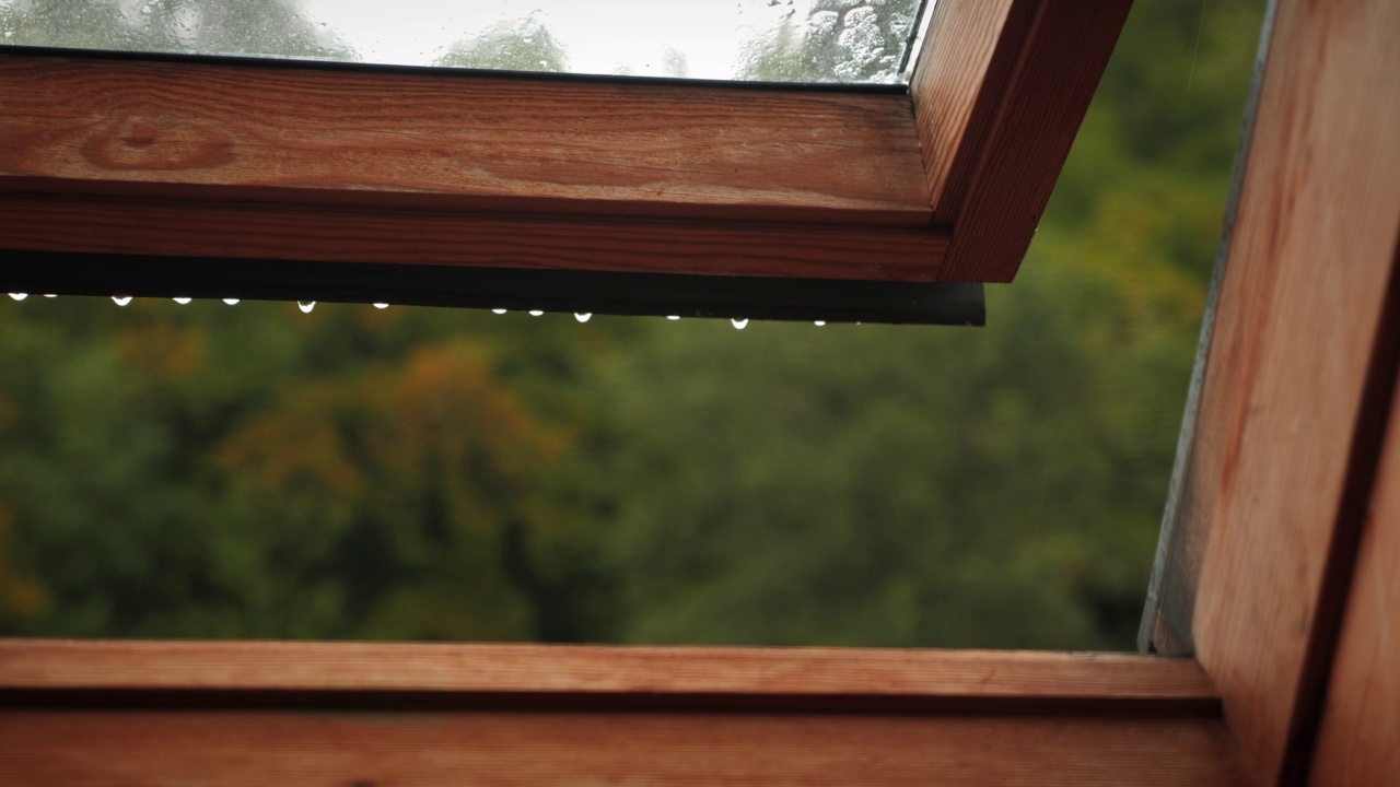 雨天，雨滴从打开的旧屋顶窗户滴下来。雨中窗户开着。寒冷的秋雨天，雨滴从敞开的窗框上落下。从打开的窗口看绿色自然景观视频素材