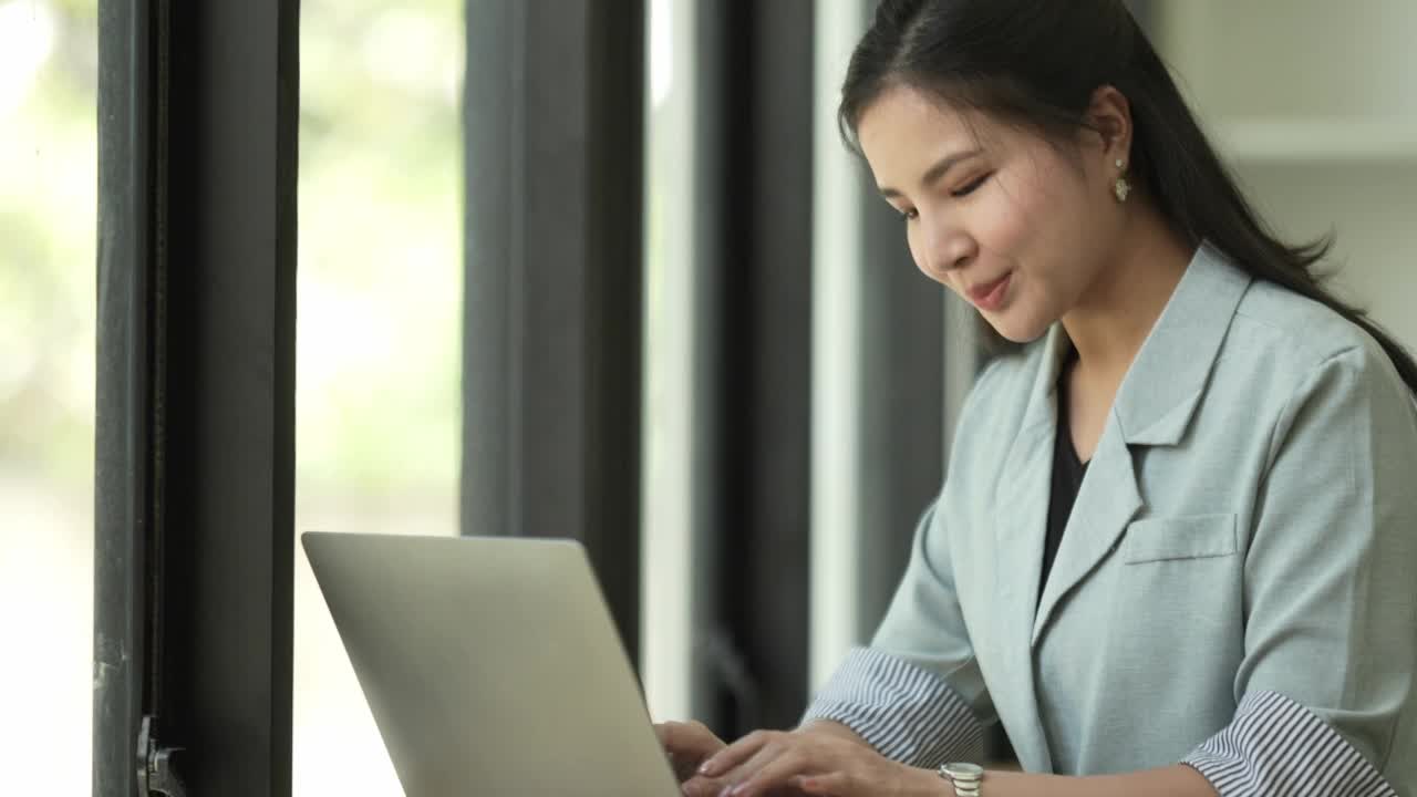 微笑迷人的年轻女子用户在笔记本电脑上打字在家庭办公室。视频素材