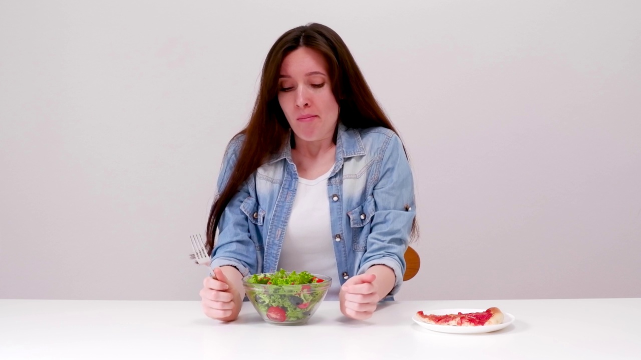 正在节食的年轻女子想吃披萨，但却选择了沙拉视频素材