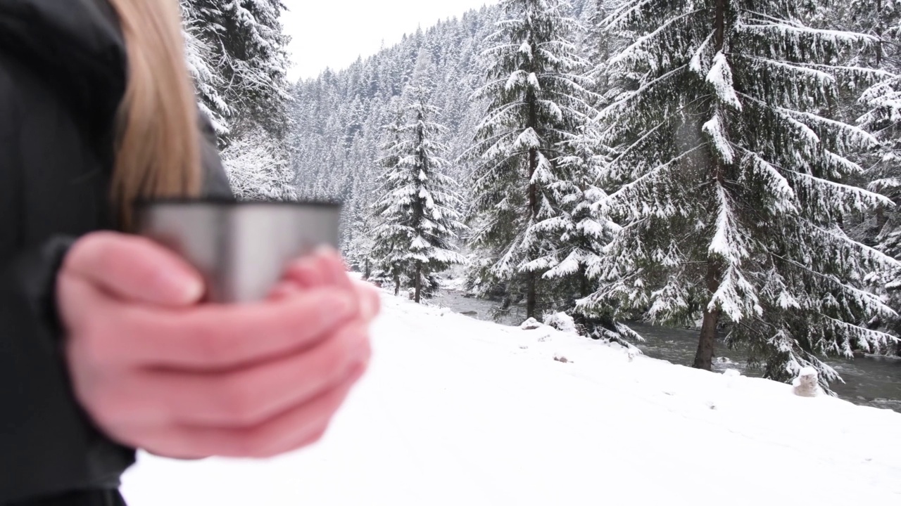 特写的女人拿着金属杯热茶在下雪的冬天森林，模糊的对象。视频素材