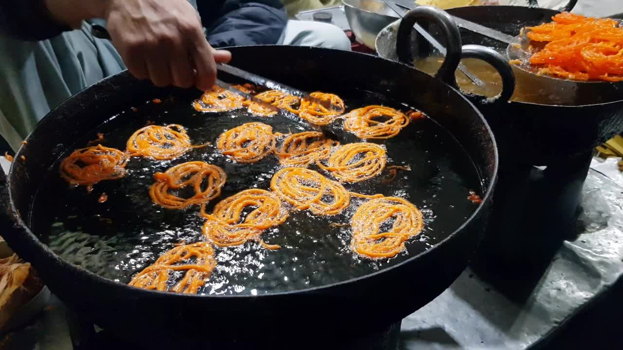 一个人在平底锅里煎甜(Jalebi)蘸甜糖浆。视频素材