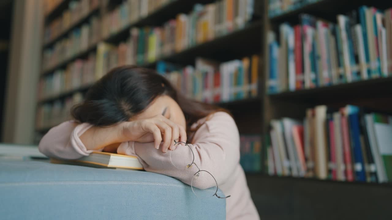 疲惫的戴眼镜的亚洲女学生睡在图书馆的书上视频素材