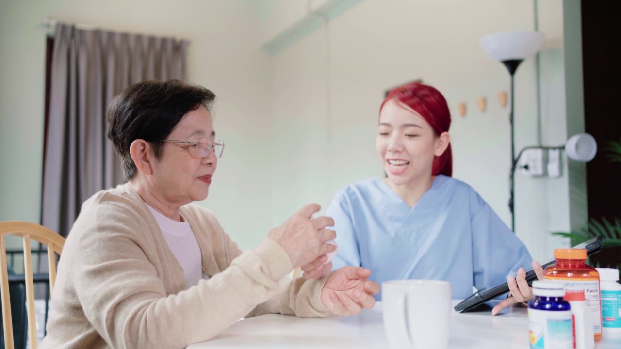 亚裔女护士拿着药瓶，在给亚裔老年妇女用药前告诉她们相关信息。护工上门拜访。家庭保健概念。4k慢动作视频。视频素材