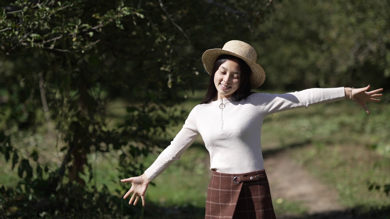 年轻快乐的女人站在阳光下伸出手开始慢动作走路。肖像的亚洲积极的女士漫步在阳光明媚的公园环顾四周微笑。休闲和欢乐的概念。视频素材