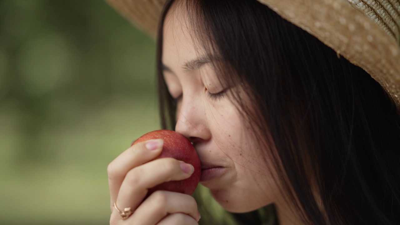 侧视图特写的亚洲妇女嗅咬健康的维生素苹果在慢动作。阳光明媚的日子，戴着牙套的积极年轻女士站在户外吃着美味可口的水果。视频素材