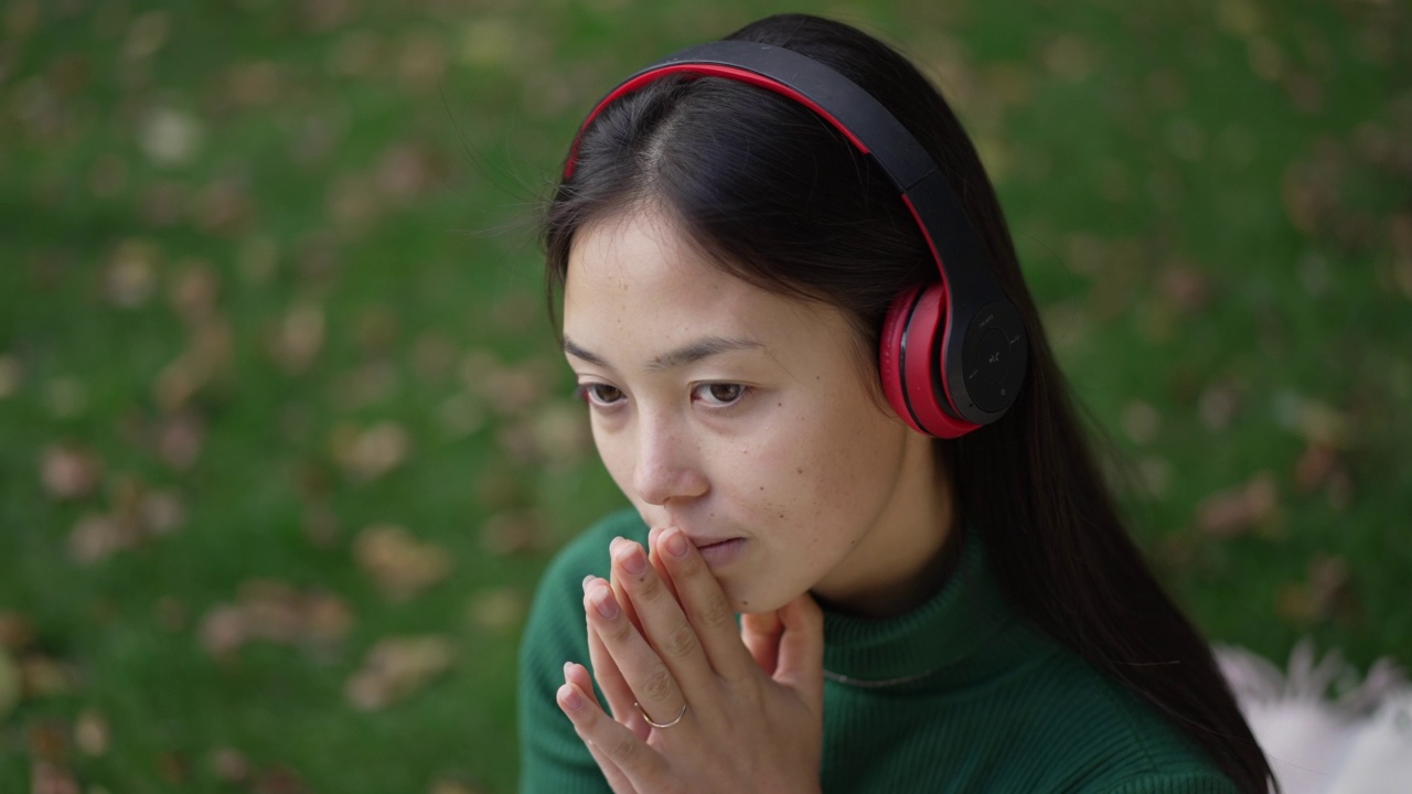 特写体贴自信的亚洲妇女听音乐摘下耳机微笑。画像迷人满足的女士享受野餐休闲夏秋公园户外。视频素材