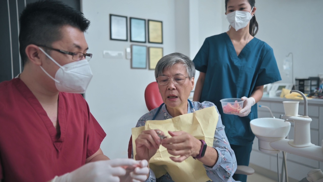 亚裔华人男性牙医展示假牙，向老年女性患者解释解决方案视频素材