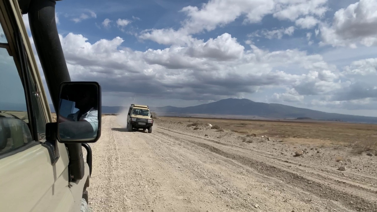 这辆SUV行驶在一条尘土飞扬的道路上，沿着荒凉的非洲大草原，载着游客。视频素材