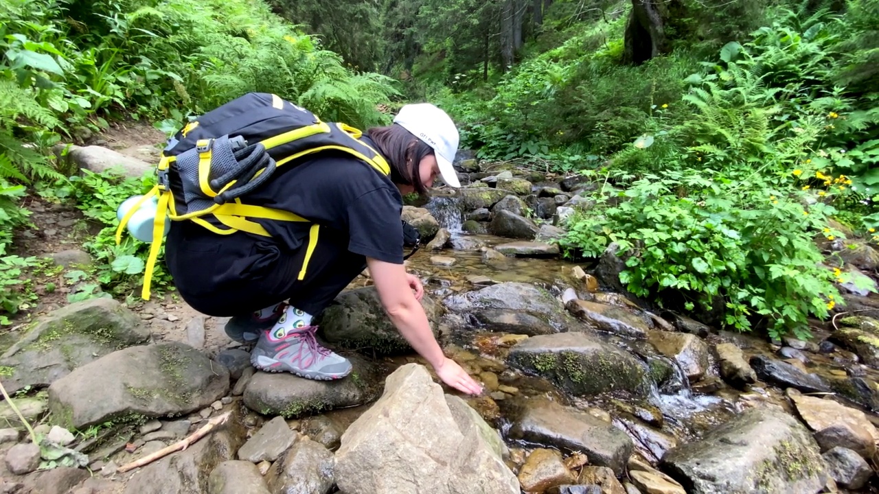 背着背包的女子徒步旅行者喝山间小溪视频素材