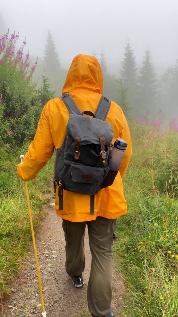 在阴天的山路上，穿着黄色雨衣的疲惫的徒步旅行者视频素材