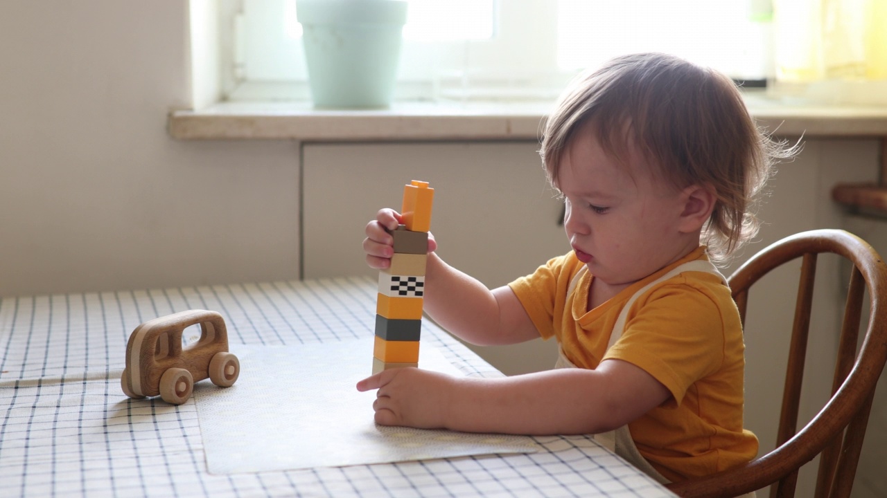 孩子一个人在桌子上玩。Child专注于用塑料积木搭一座塔视频素材