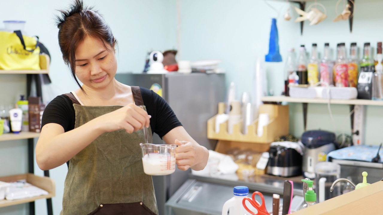 年轻女子用勺子把牛奶倒入量杯中视频素材