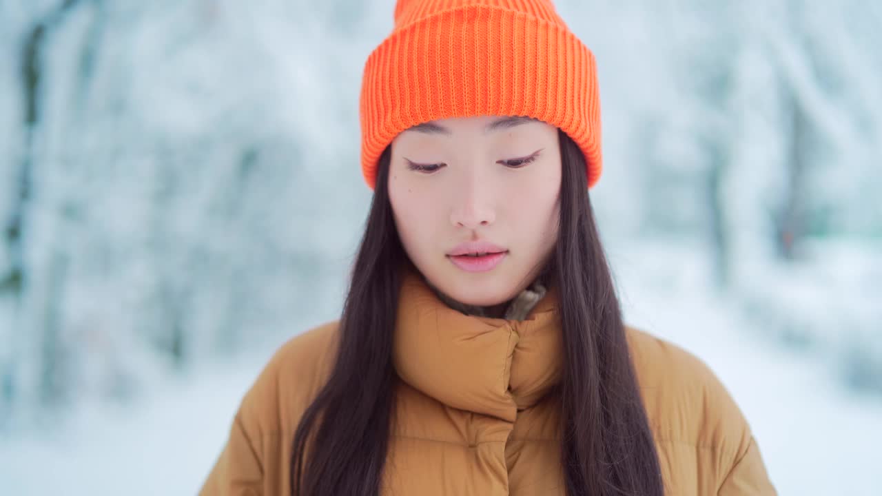 美丽的肖像年轻的亚洲妇女站在雪地背景在公园在寒冷的天气，看着相机。面对年轻快乐的微笑美丽的女孩在冬天的户外视频素材