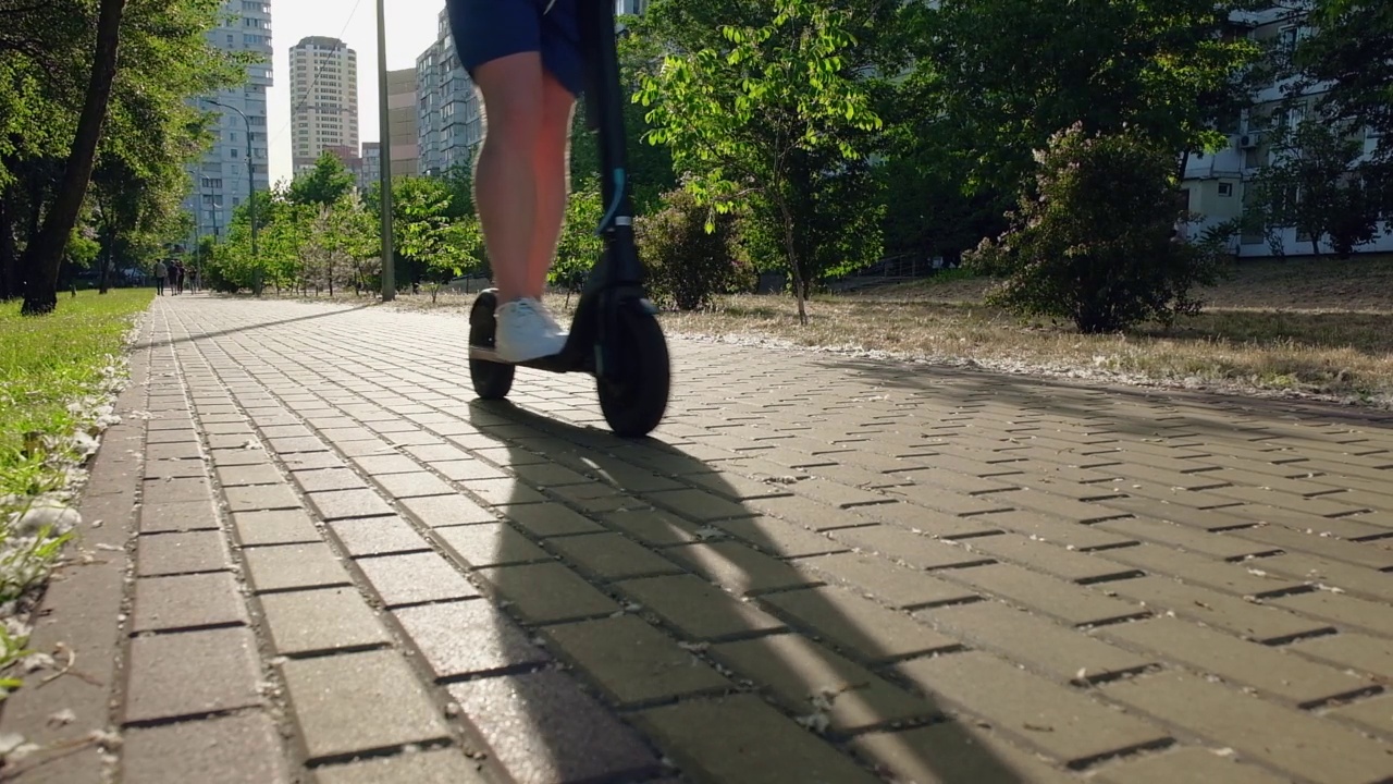 在一个阳光明媚的日子里，一名男子骑着电动摩托车在城市道路上行驶。城市生活方式，生态交通视频素材