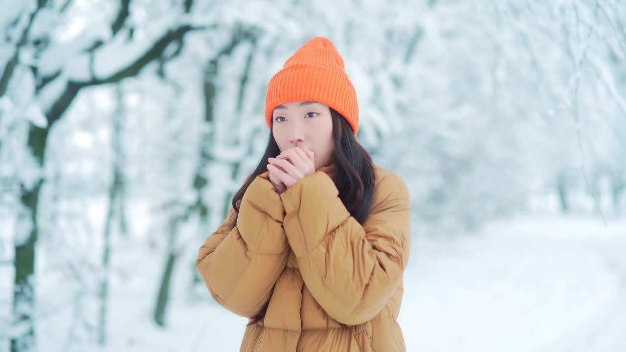 一个年轻的亚洲女孩在公园里等待约会，在一个冬天的雪天，一个穿着暖和的女人。女性的肖像冻结，寒冷的天气在雪地背景的户外视频素材